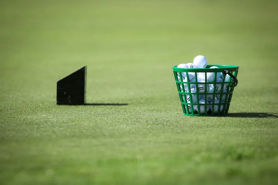 Wire basket of practice golf balls beside a tee marker on driving range grass