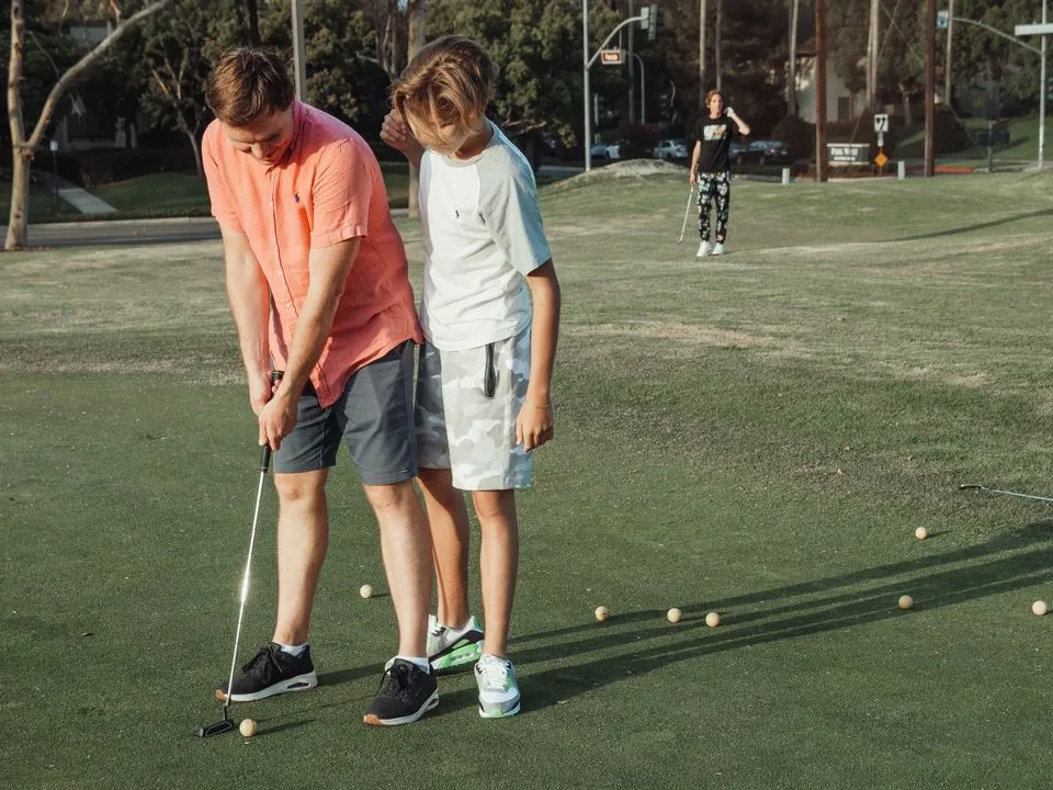 Father putting on a practice green while his son watches, balls scattered around them